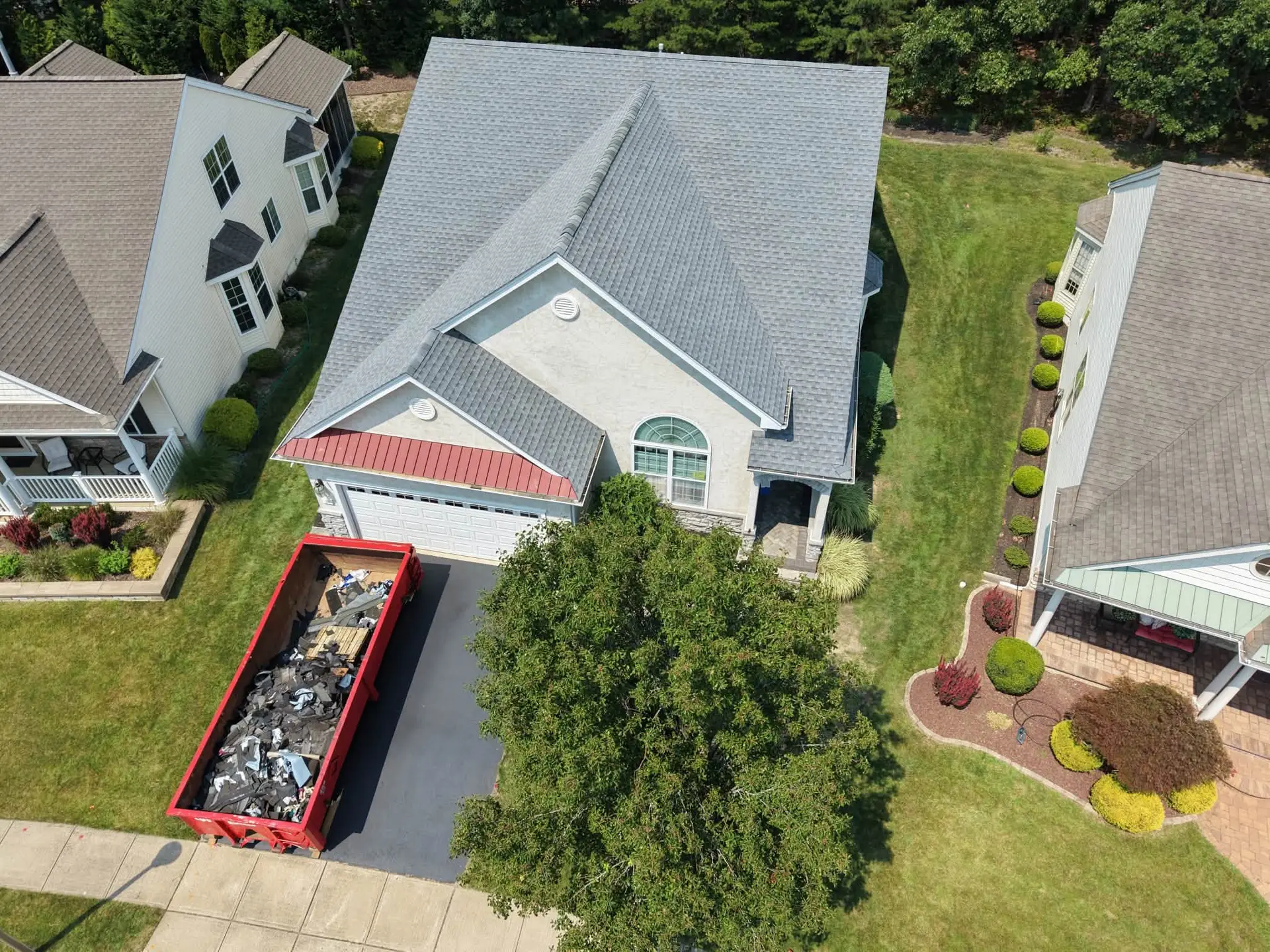 Aerial view of a roof replacement in progress with a red debris container in the driveway of a New Jersey home