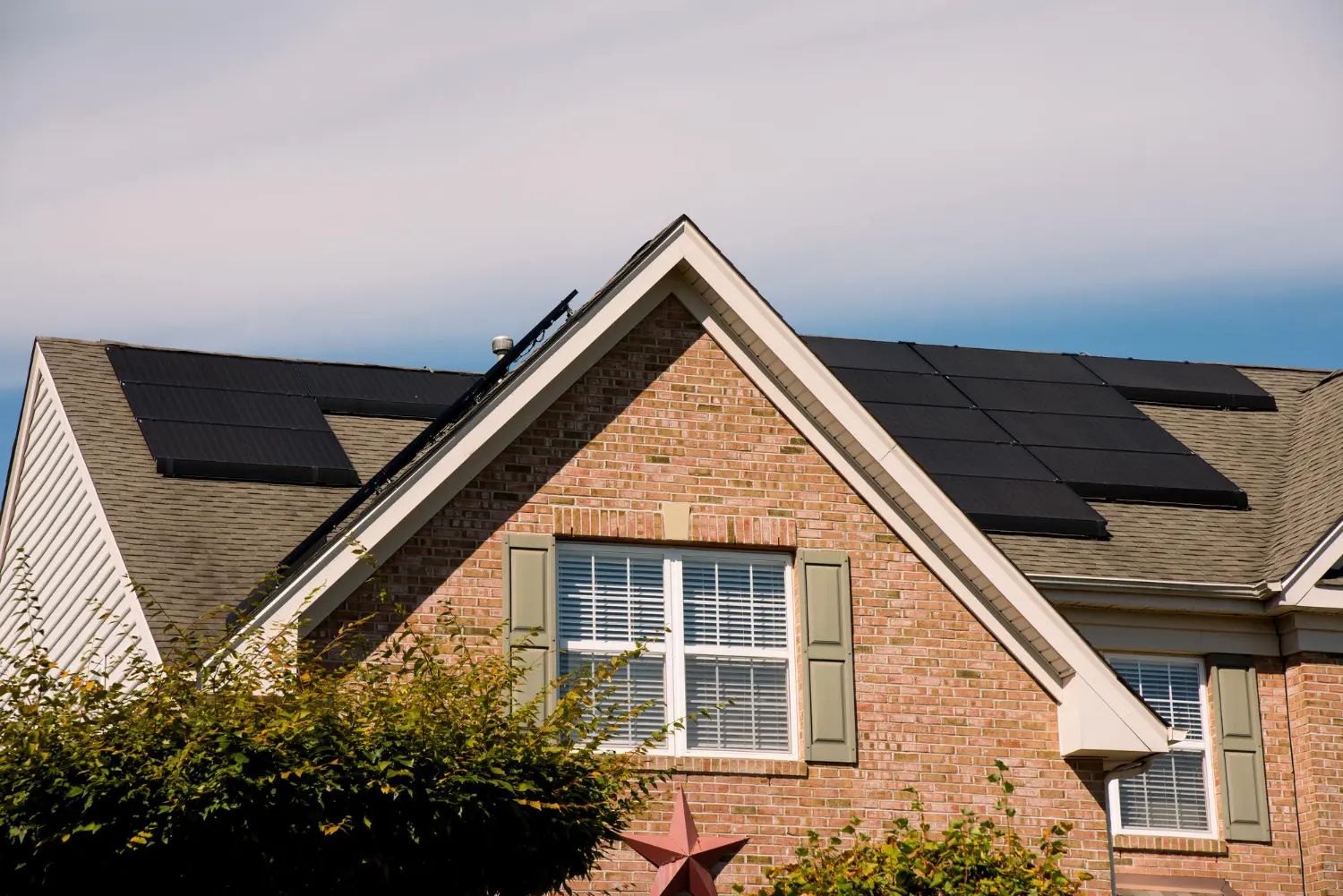 Black solar panels installed on the gray shingle roof of a red brick home in Ocean County, NJ